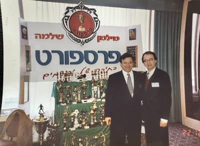 שני גברים בחליפות מול דוכן פרספורט עם גביעים