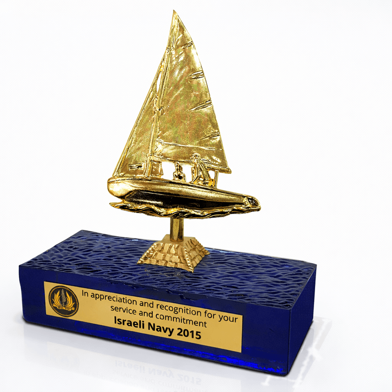 מגן הוקרה לחיל הים עם פסלון מפרשית זהב על בסיס זכוכית כחולה בטקסטורת גלים ופלטת הקדשה אישית.